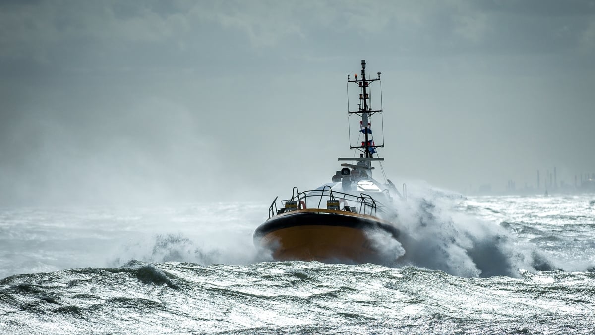 Rescue vessel powering through rough seas during a storm with waves crashing over the bow.